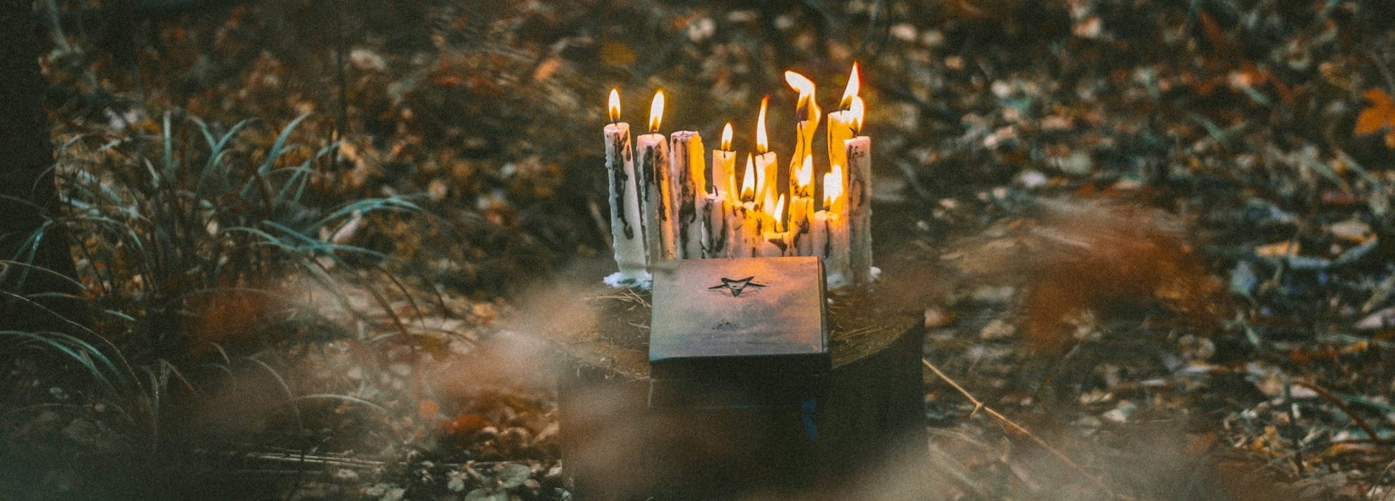 A photo of some lit candles and a paper with a star on it set out as an offering on a tree stump.